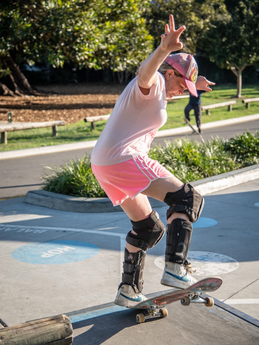 A woman wearing a pink t-shirt and hat is performing a skateboarding trick on a skate ramp.