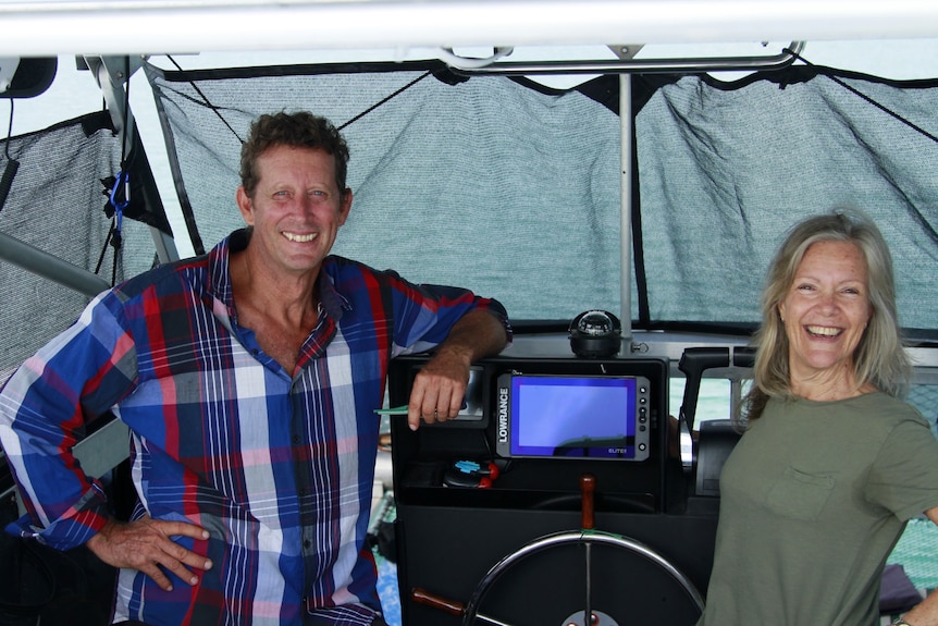 Middle aged man and woman stand on a boat next to steering wheel and screen