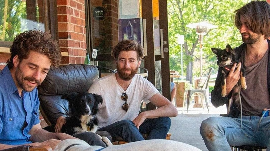 The three brothers smile while looking at their dogs, seated outside the cafe.