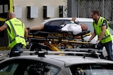 A man lies on a stretcher being wheeled be two emergency services workers in high vis.