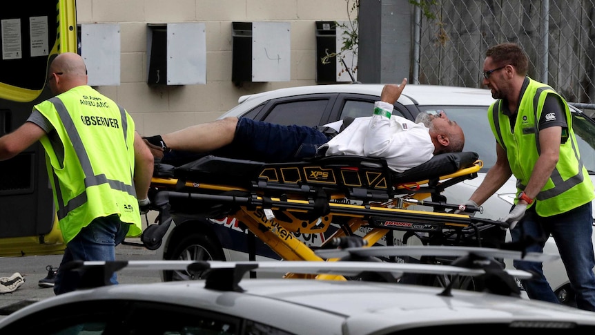 A man lies on a stretcher being wheeled be two emergency services workers in high vis.