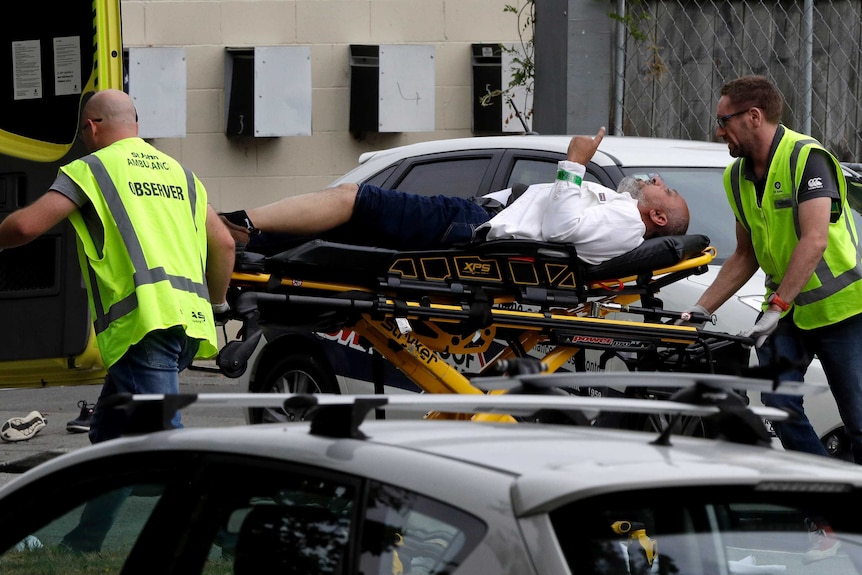 A man lies on a stretcher being wheeled by two emergency services workers in high vis.