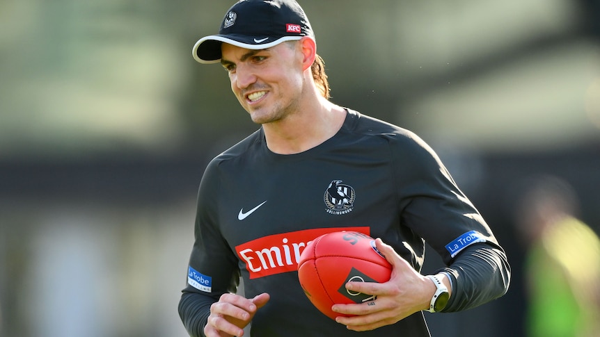 Brayden Maynard smiles while holding a football at Collingwood training