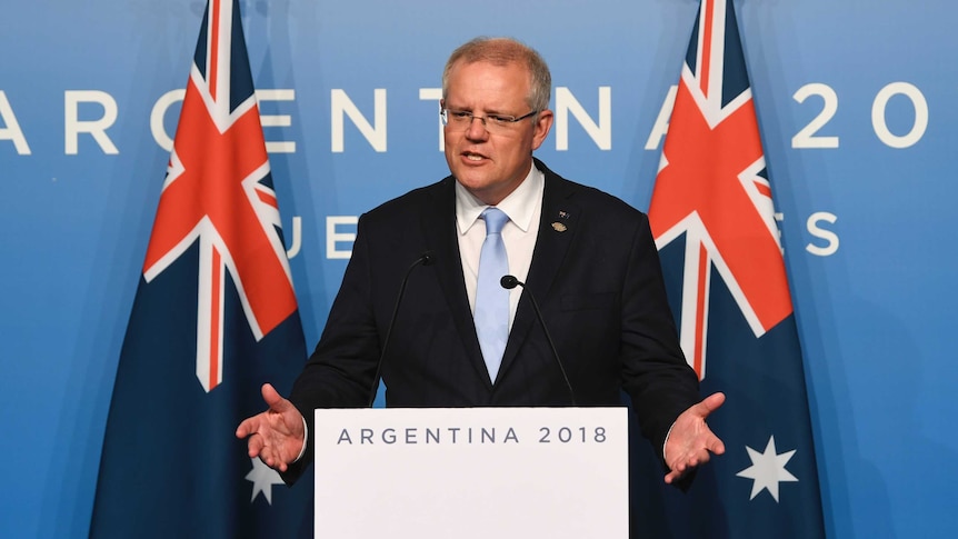 Scott Morrison, standing in front of two Australian flags, gestures with his hands.