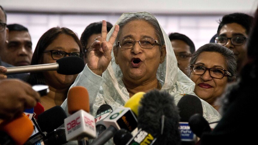 Sheikh Hasina holds up two fingers in a victory sign as she speaks to the media pack around her.