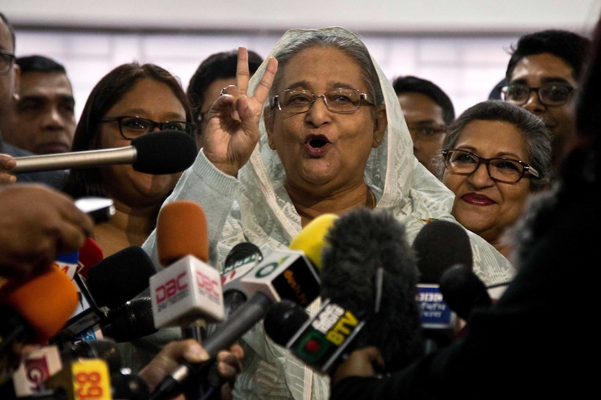 Sheikh Hasina holds up two fingers in a victory sign as she speaks to the media pack around her.