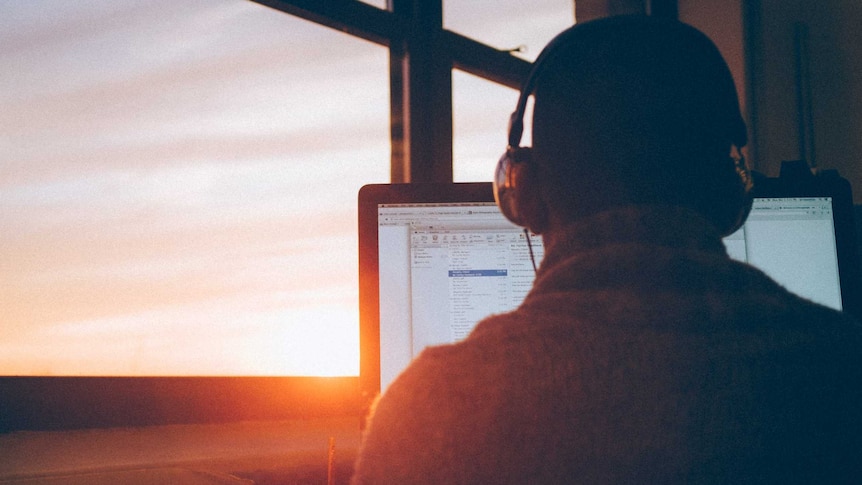 A man in headphones working on a computer as the sun beams through his window
