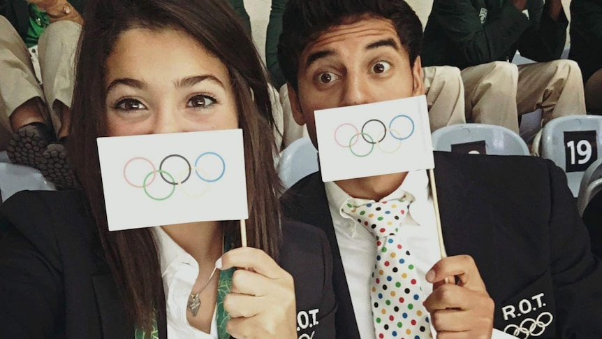 Refugee Olympic Team swimmers Yusra Mardini and Rami Anis wearing Olympic Jackets and holding flags at the opening ceremony.