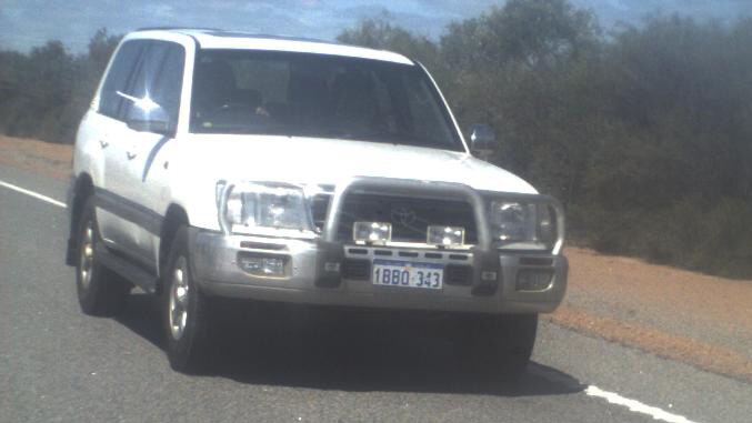 A white Toyota Landcruiser driving on a country road during the day.