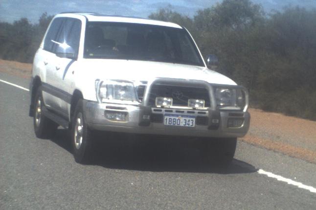 A white Toyota Landcruiser driving on a country road during the day.