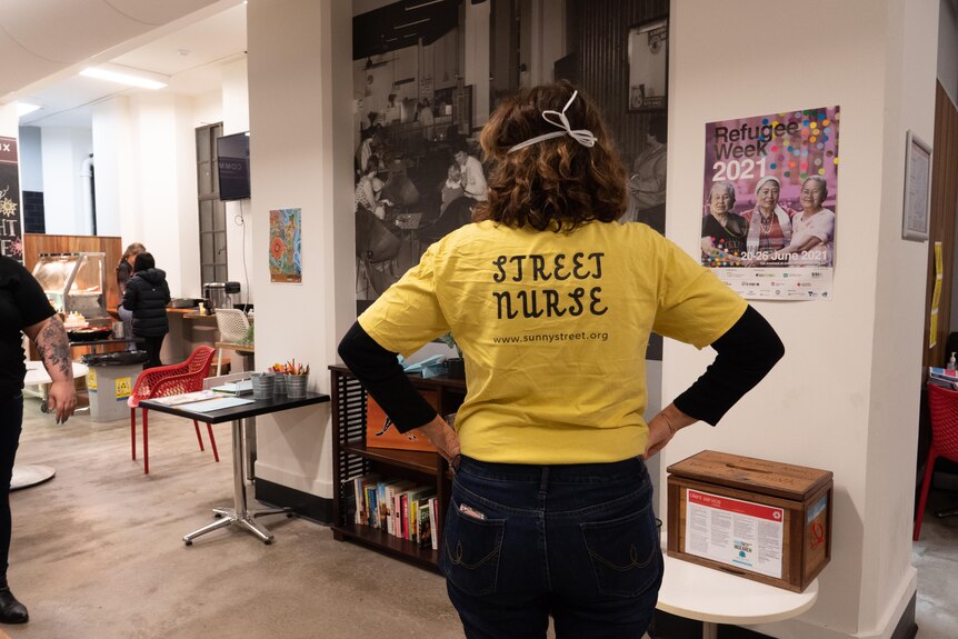 The back of a woman wearing a bright yellow t-shirt that reads "street nurse".