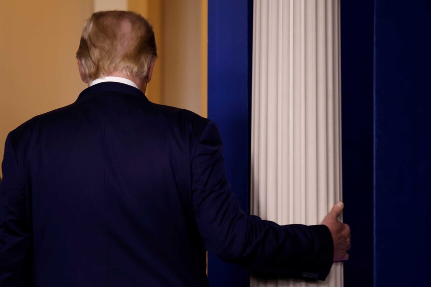 A behind view of Trump as he grabs an architectural column