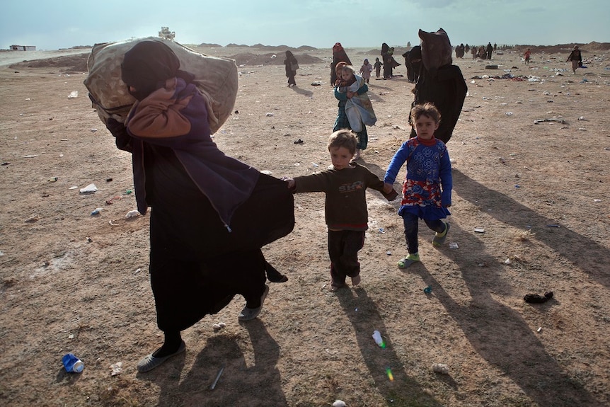 A woman carries a laden sack on her right shoulder as she is trailed by two children who are holding hands