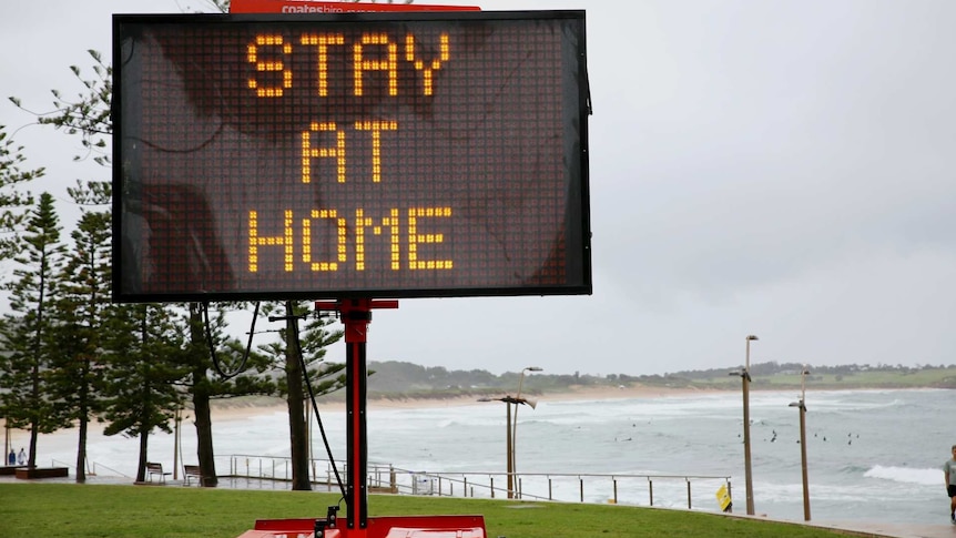 a stay at home sign on a beach front