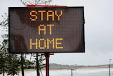 a stay at home sign on a beach front