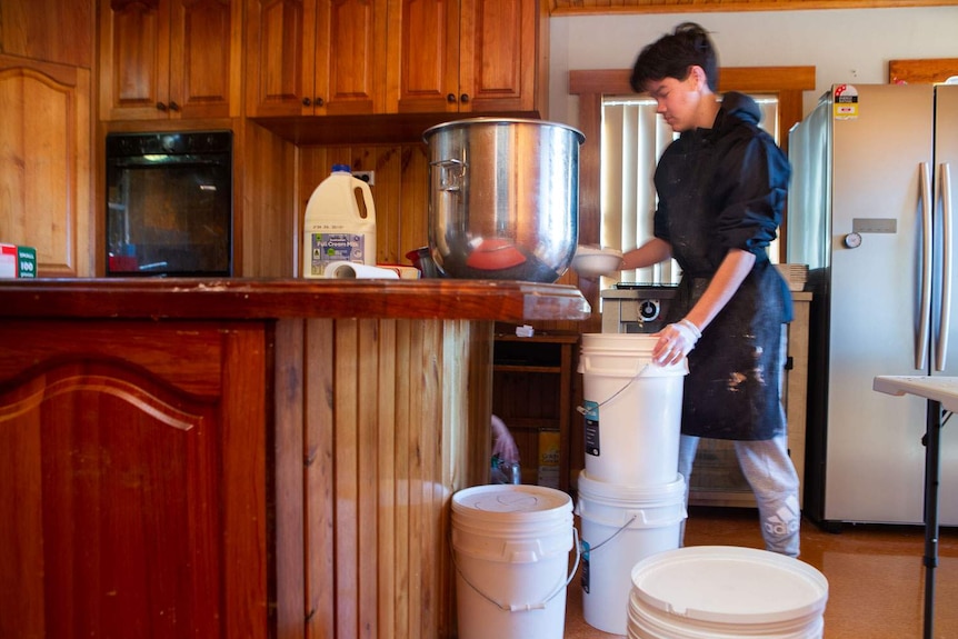 Sunny measure out flour, surrounded by large buckets of flour, yeast and other ingredients in the kitchen