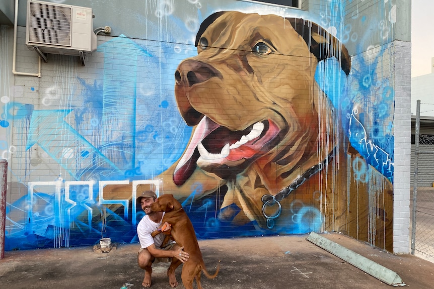 a young man and a dog in front of street art