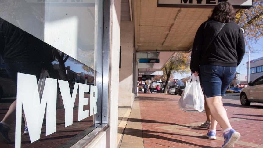 A window sign saying MYER in black and white with pedestrians walking by on the footpath