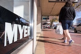 A window sign saying MYER in black and white with pedestrians walking by on the footpath
