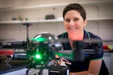 Dr Karen Joyce peers at the camera from behind a drone in her indoor hangar at James Cook University's Cairns campus.