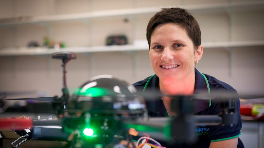 Dr Karen Joyce peers at the camera from behind a drone in her indoor hangar at James Cook University's Cairns campus.