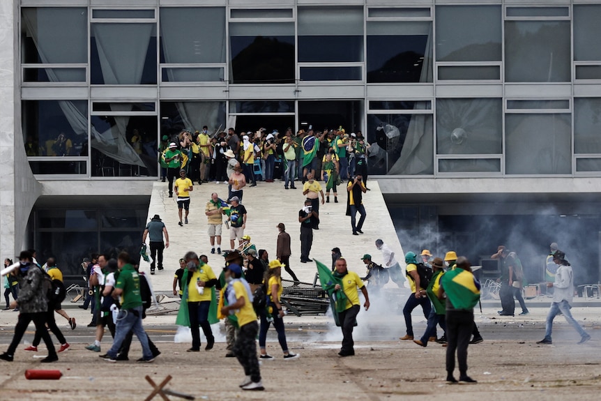 People dressed in yellow and green hold flags and surround a building.