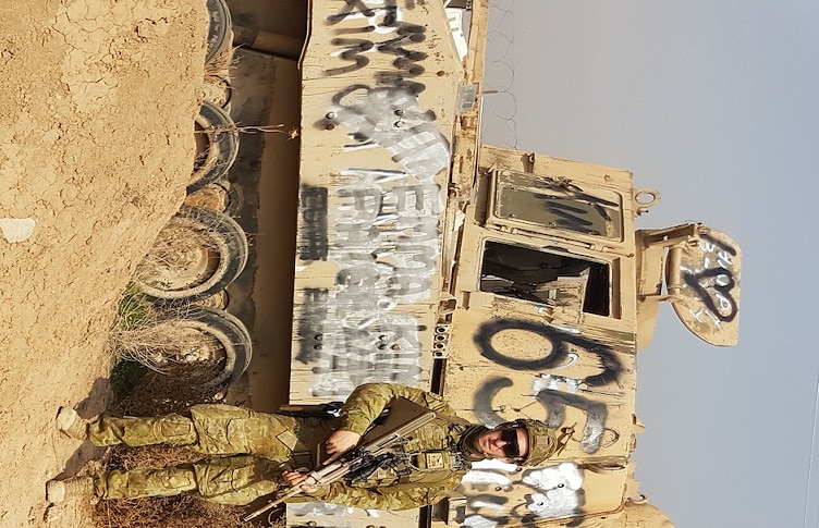 Brett Humphrey stands in army gear next to a tank.