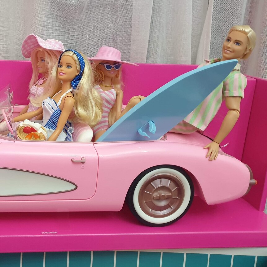 four barbie dolls and one ken doll in a pink toy car