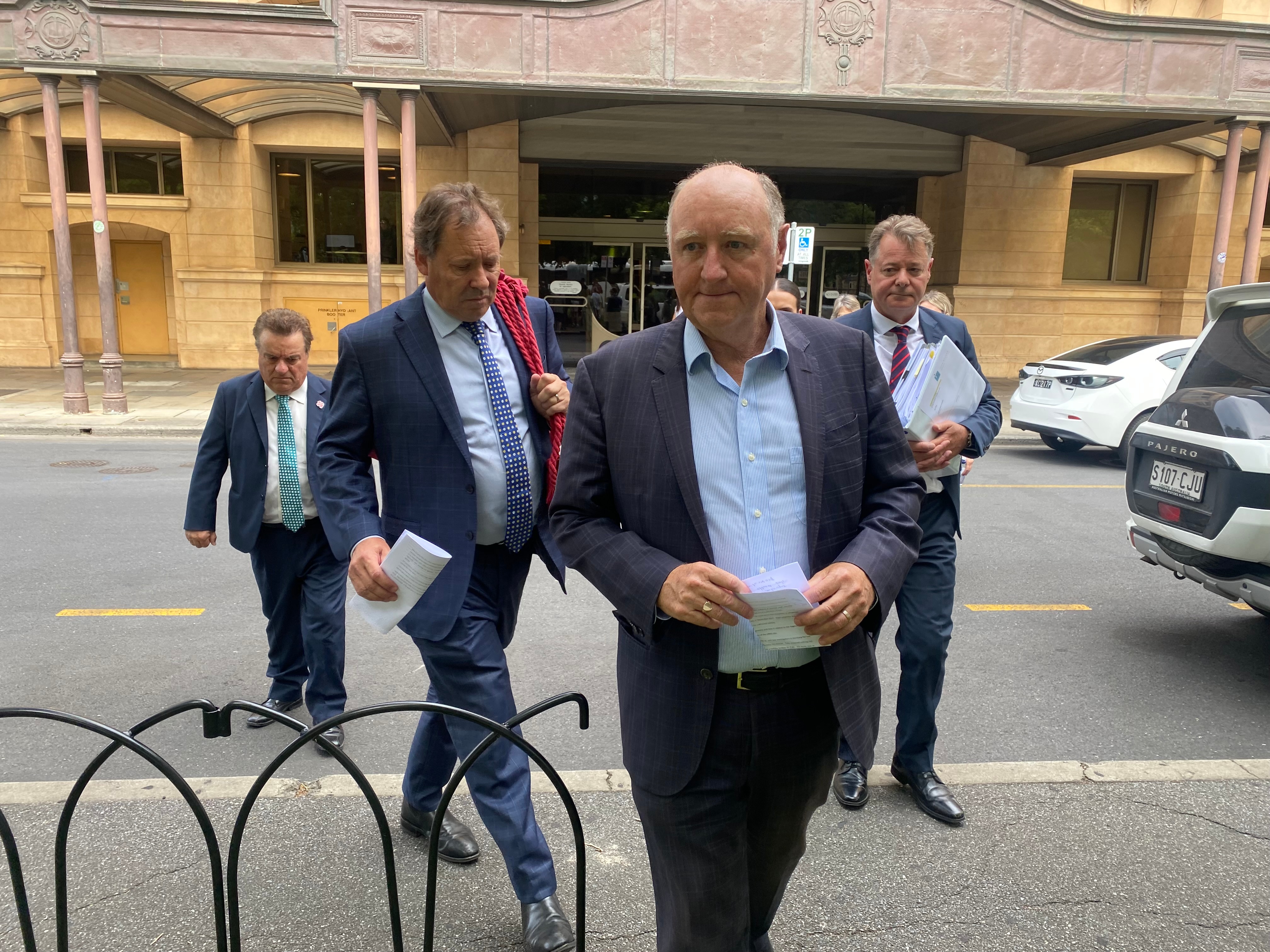 A group of men wearing suits walk across a road