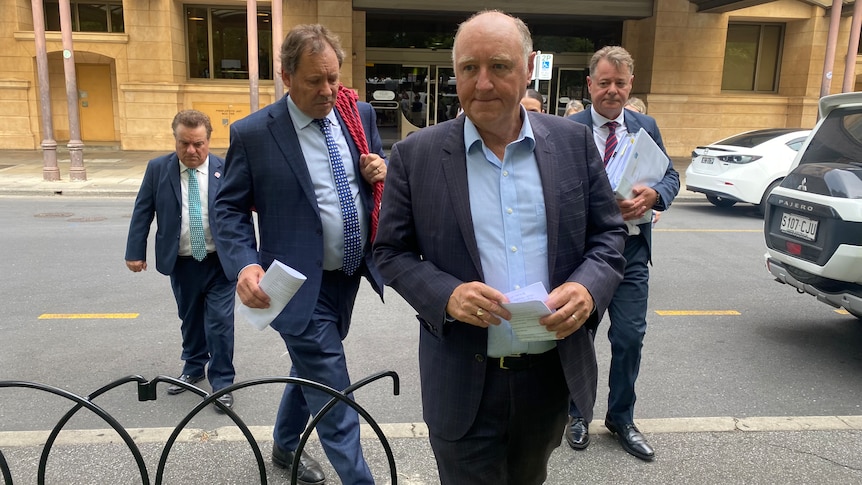 A group of men wearing suits walk across a road