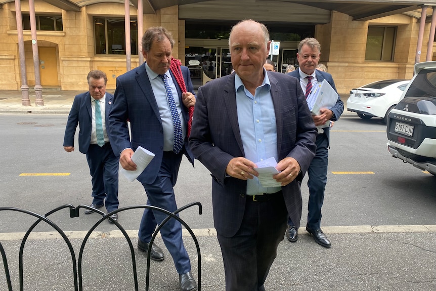 A group of men wearing suits walk across a road