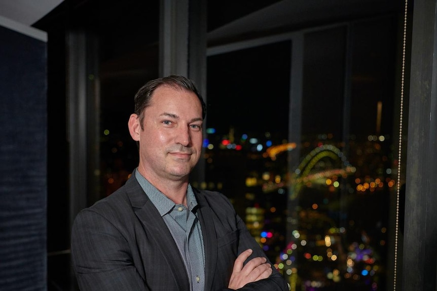 A man standing in front of a window and smiling to camera