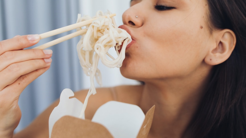 Woman eating noodles with chopsticks straight out of a takeaway container