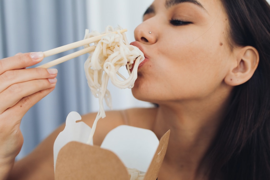 Woman eating noodles with chopsticks straight out of a takeaway container