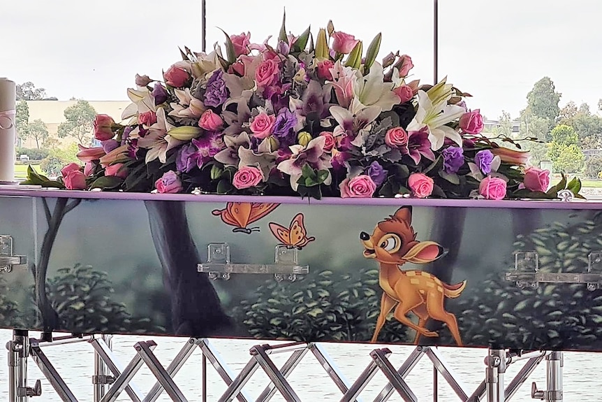 A coffin with a flower on the top and a painted picture of deer.