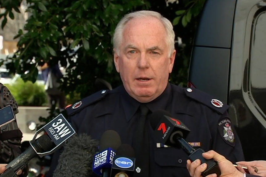A man with grey hair and in a police uniform speaks to media.