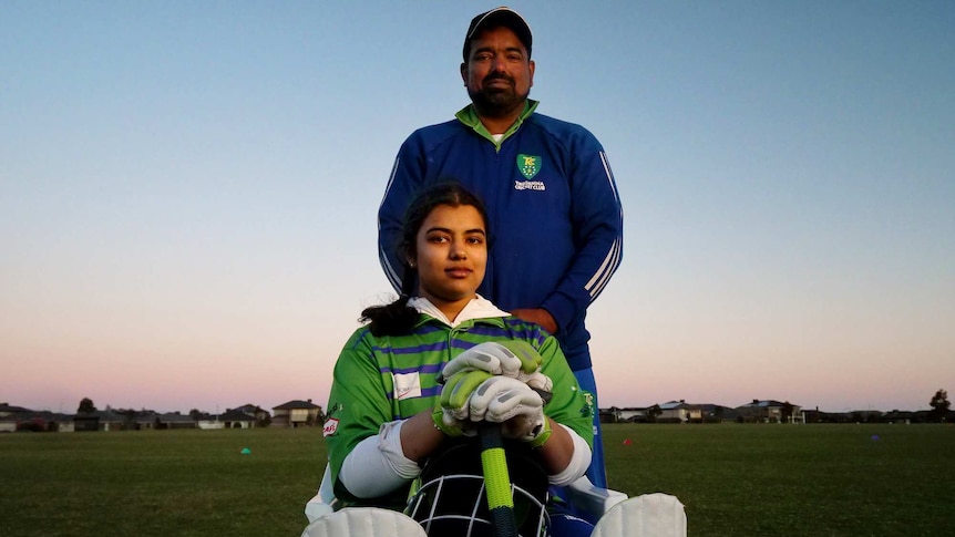 Jamal Mohammed stands behind his daughter, who is dressed in a cricket jumper holding a bat.