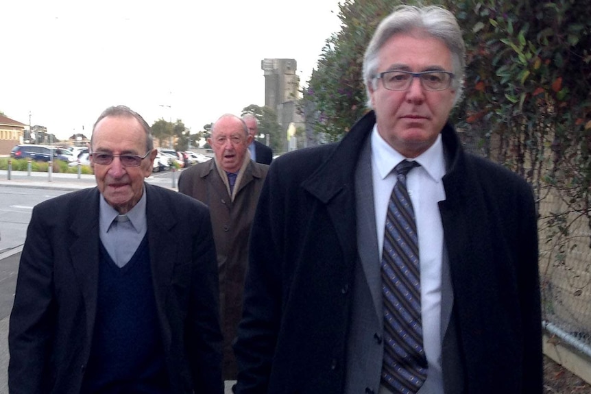 Two men in suits walk side by side with another following behind