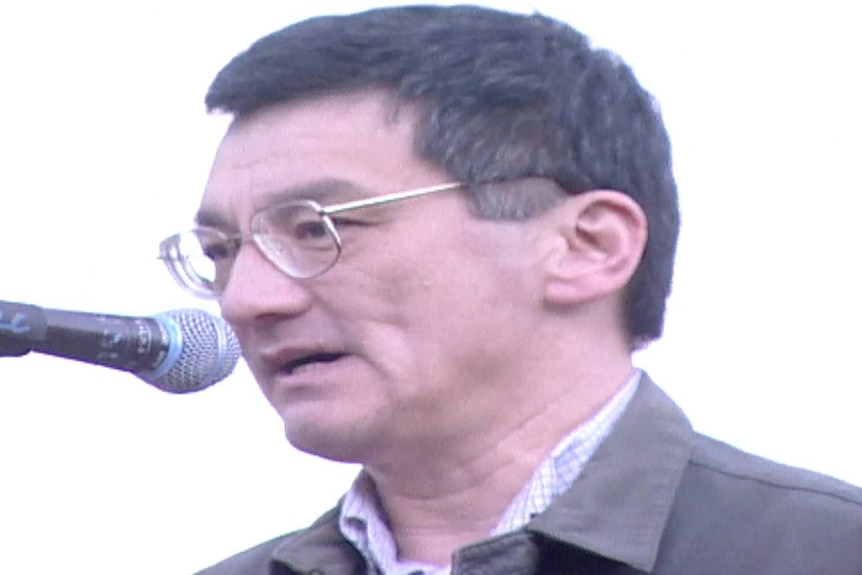 A headshot of Tsebin Tchen speaking into a microphone at a community event.