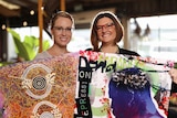 Two women stand together holding up examples of graphic design work.