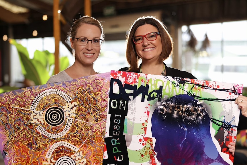 Two women stand together holding up examples of graphic design work.