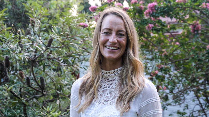 Mindy Woods wearing a white shirt standing in front of trees. 