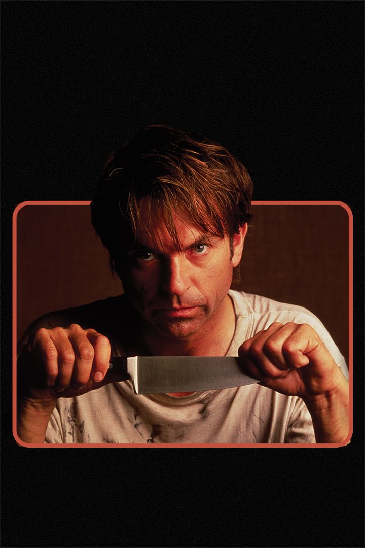 a man stares forwards, holding a knife by the handle and the blade