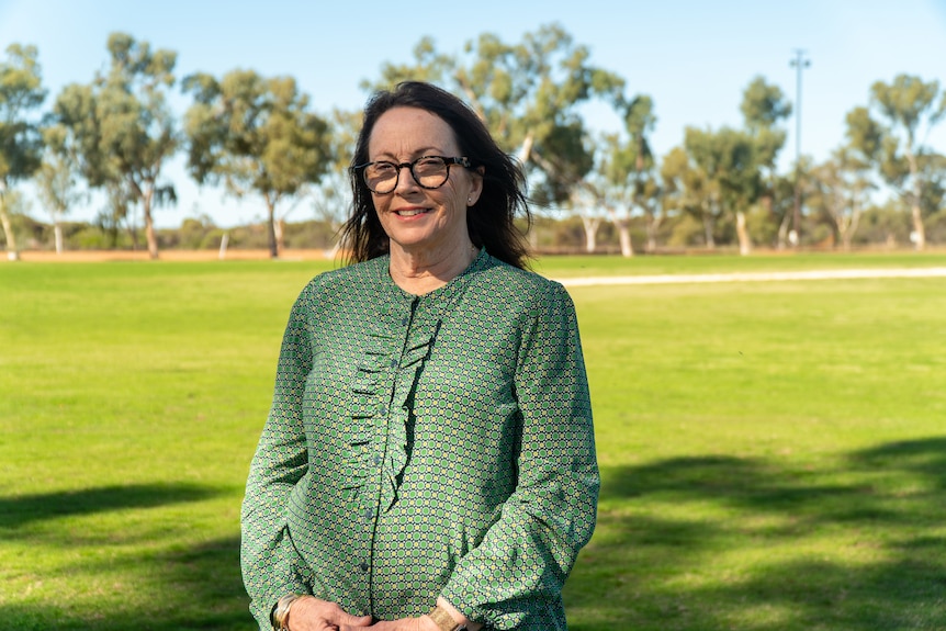 a woman with dark hair in a green shirt standing in a park 