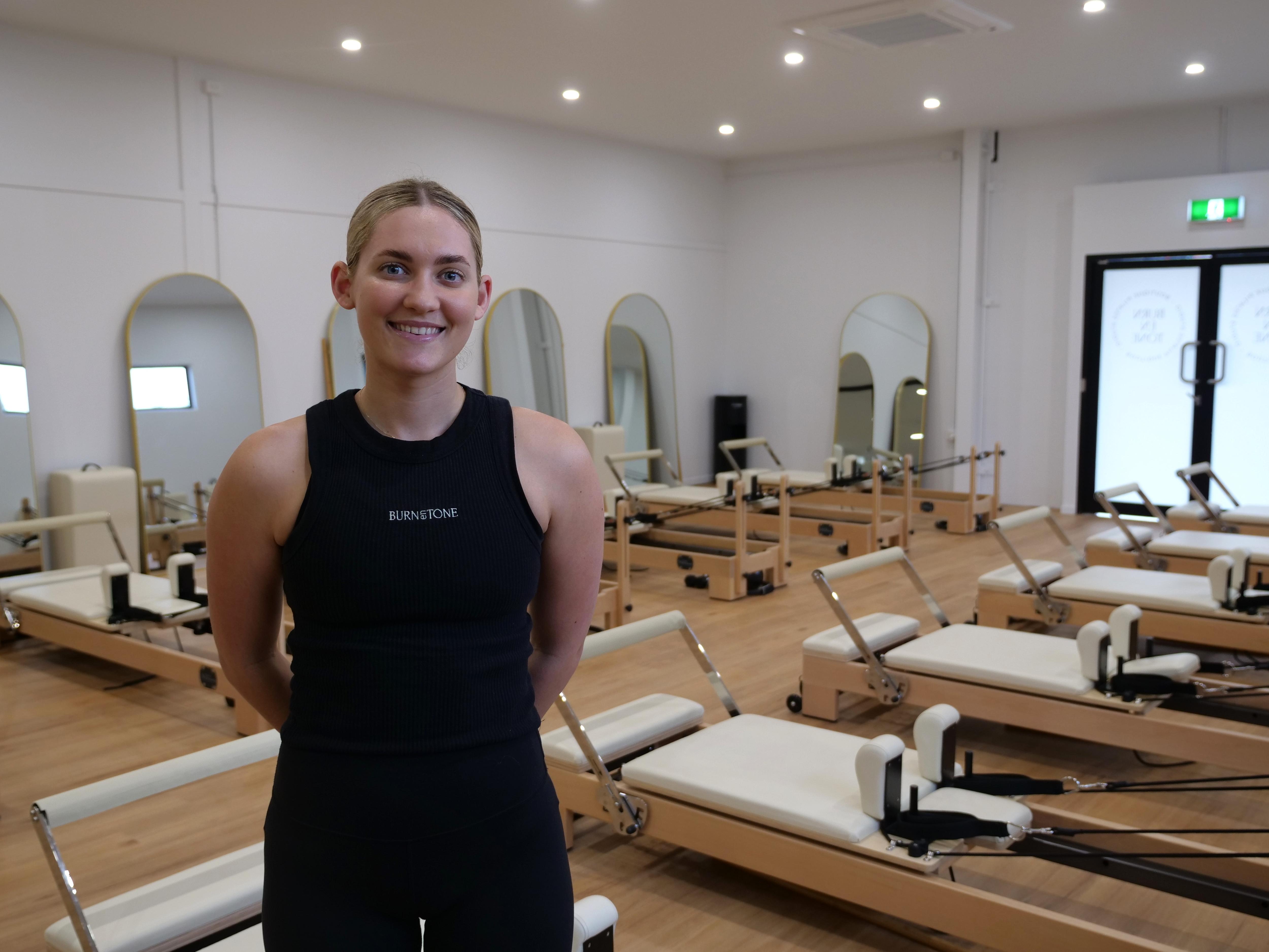 Young woman wearing black activewear standing in a pilates reformer pilates room. 