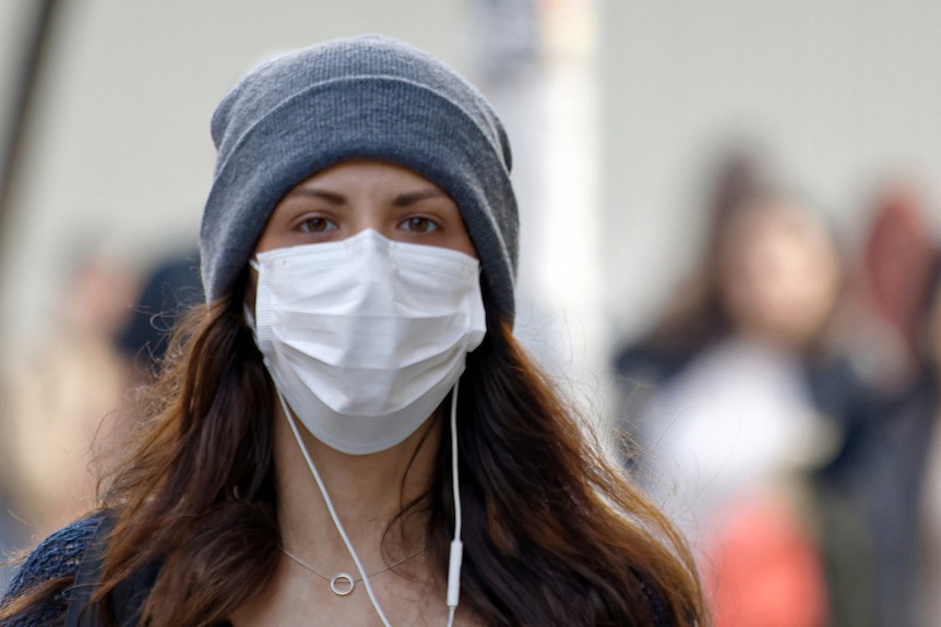 Young woman wearing a mask and beanie in outdoor setting.