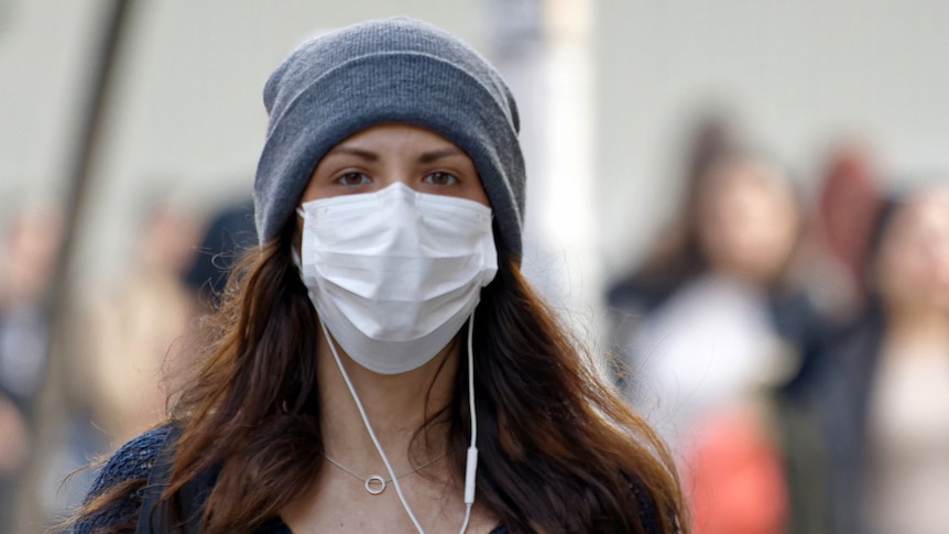 Young woman wearing a mask and beanie in outdoor setting.