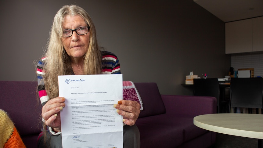 An older woman sits on her coach holding up a letter from VincentCare