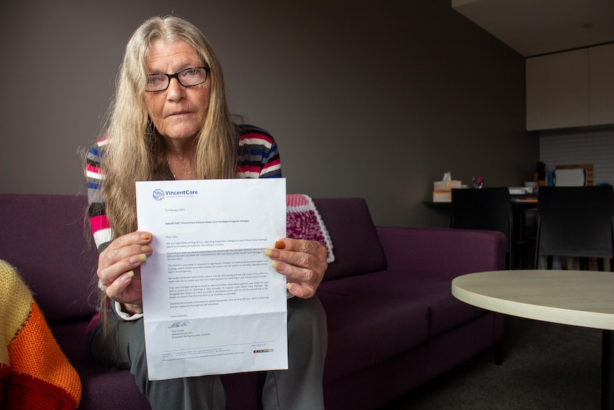 An older woman sits on her coach holding up a letter from VincentCare