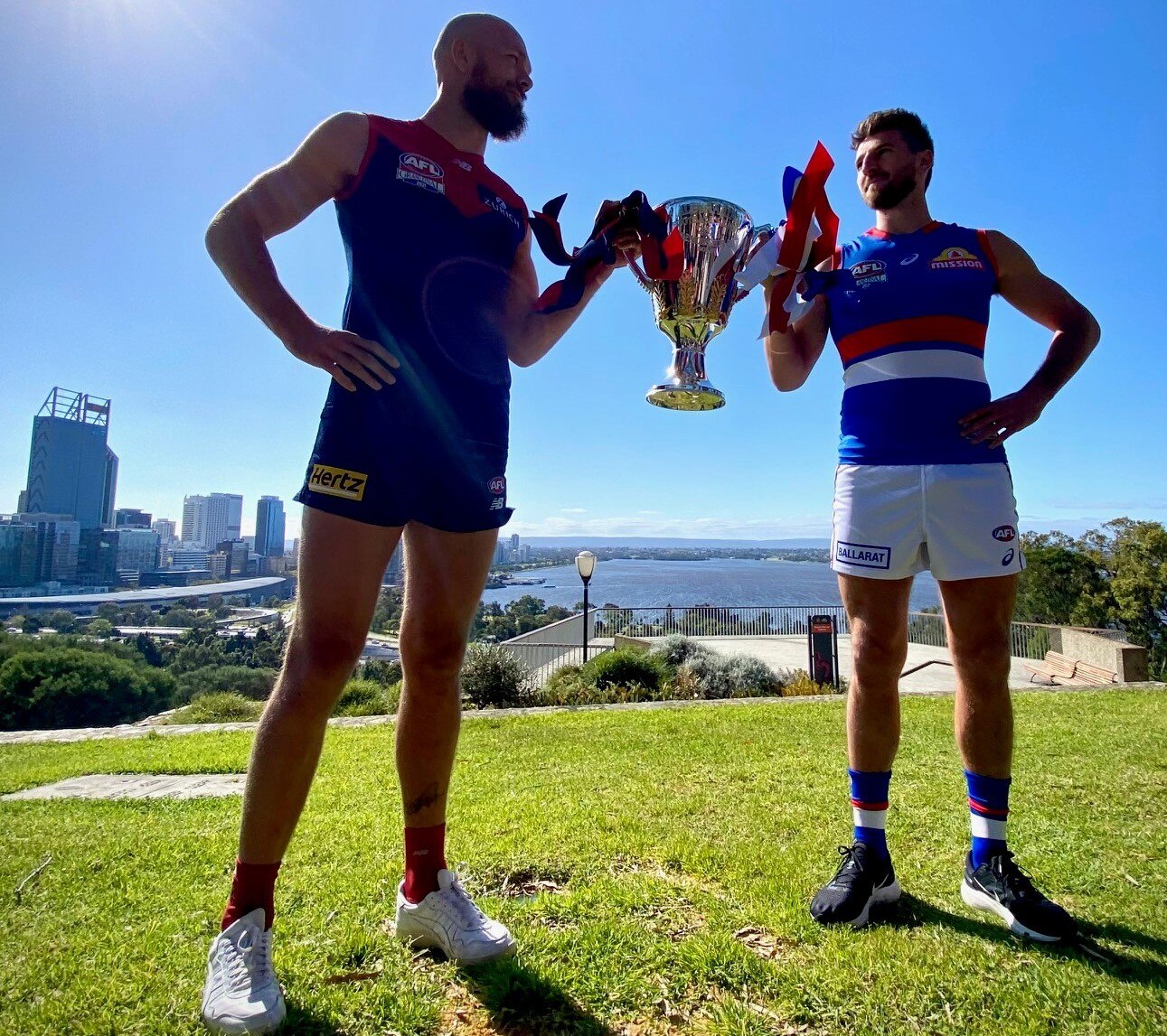 Demons captain Max Gawn and Bulldogs captain Marcus Bontempelli face each other while holding the cup